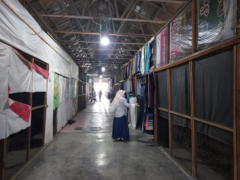 A woman touches some pants in a market stall. There are empty stalls around her.