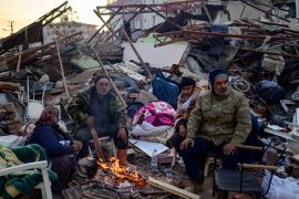People stand by a fire among the rubble of collapsed building in Hatay, on February 10, 2023, four days after a 7.8 magnitude earthquake