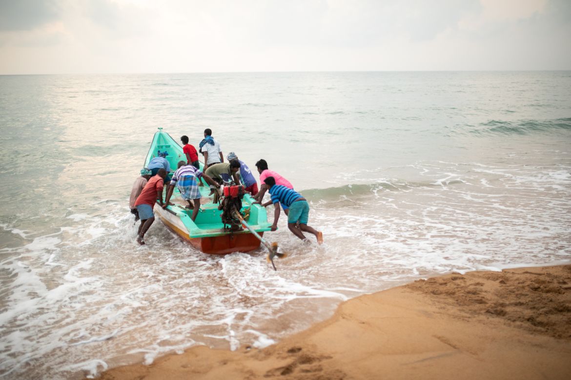 A photo of people pushing a boat into the ocean.
