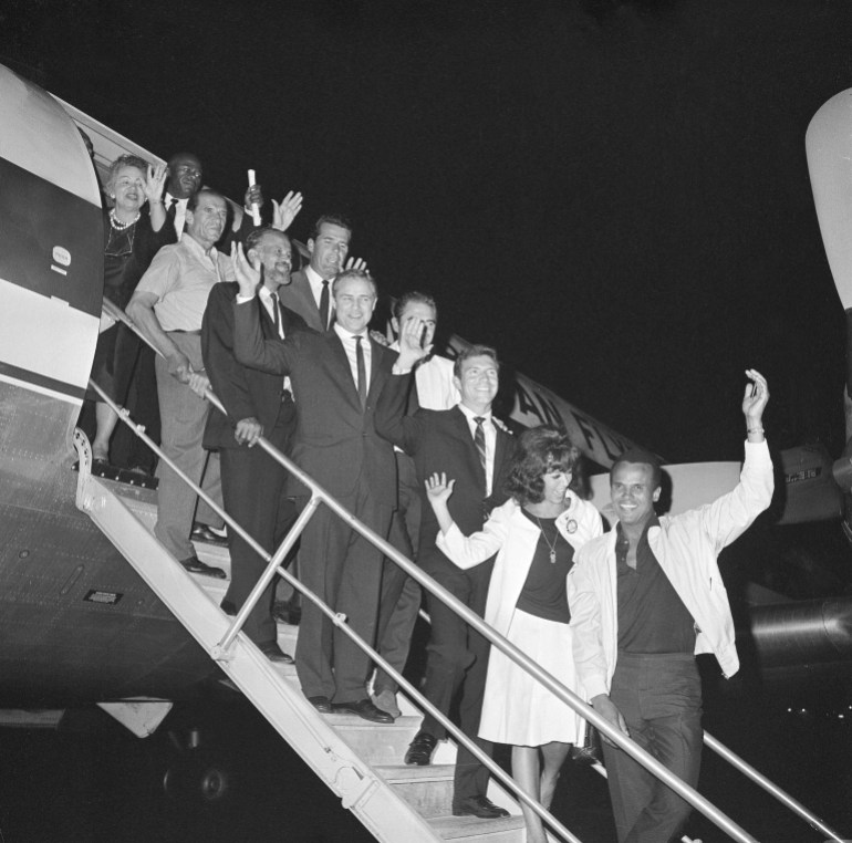 Hollywood celebrities pose on the steps of a plane in 1963