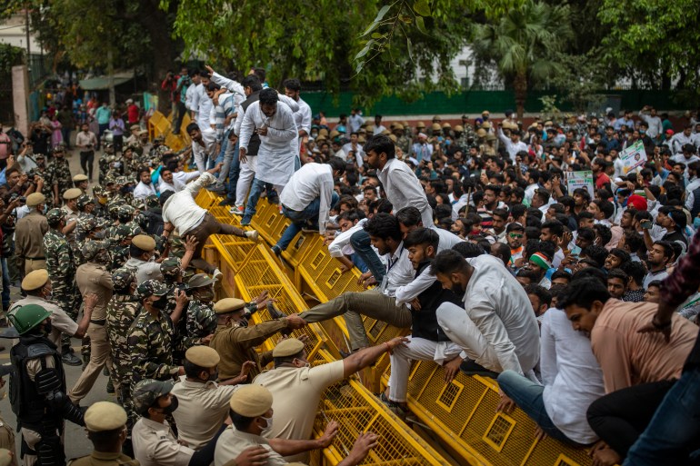 Indian police officers try to pull down members of National Students Union of India (NSUI), the student body of the Congress party, who climbed on police barricades during a protest against rising unemployment in the country in New Delhi, India, Friday, March 12, 2021. (AP Photo/Altaf Qadri)