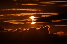 A partial solar eclipse rises behind clouds