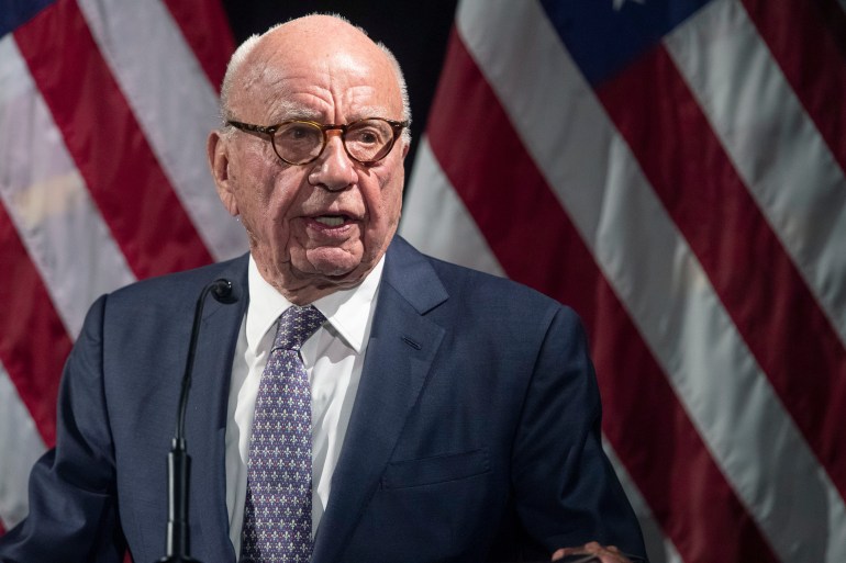 Rupert Murdoch, seen in a suit and tie in front of a US flag