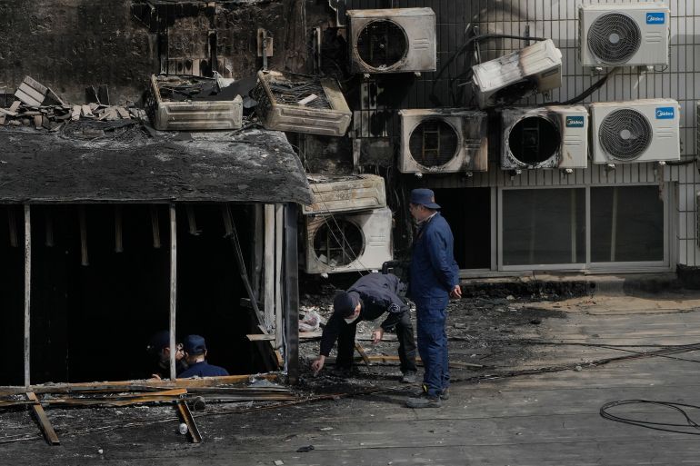 An investigator bends down to look at something on the ground at the scene of the Beijing hospital fire. There are numerous airconditioners on the wall of the building and some have been destroyed by the fire. There is soot on the walls.