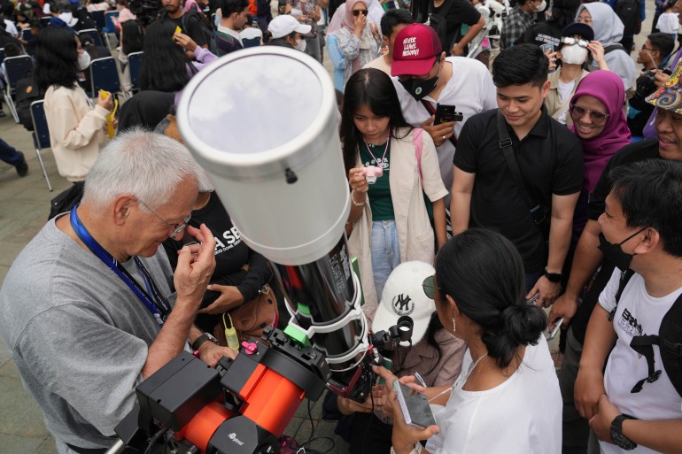 People gathered around a large telescope in Jakarta as they take turns to view the partial solar eclipse, Some are children.