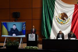 A screen positioned in front of Mexico's lower chamber of Congress, with a big Mexican flag draped against the wall