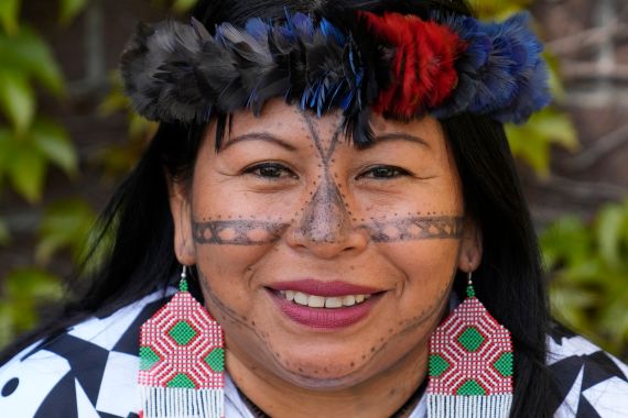 A close-up of Indigenous activist Alessandra Korap, winner of the 2023 Goldman Environmental Prize. She is wearing beaded earrings in green and pink and an ornate traditional headdress made from colourful feathers.
