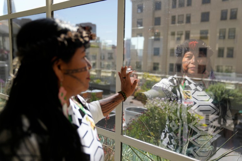 Alessandra Korap, winner of the 2023 Goldman Environmental Prize, looks out the window of a hotel, holding her hand up against the glass pane.