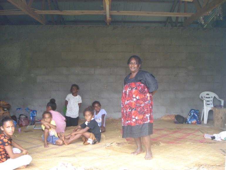 Rebecca standing on a mat in a temporary home after last month's twin cyclones. There are children sitting on the mats.