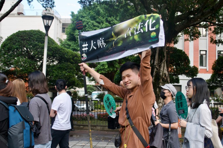 Protestors marching in Taiwan. One young man, perhaps the age of a college student, in a brown shirt is holding up a banner with both his arms.