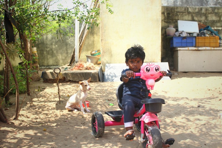 A photo of a child in a little tricycle with a dog behind him.