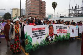 Protesters march down a road with a banner featuring a photo portrait of Eduardo Mendua, with a timespan representing his life: 1982-2023