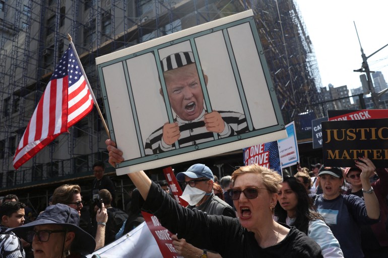 A woman holds up a hand-drawn sign showing Trump behind bars