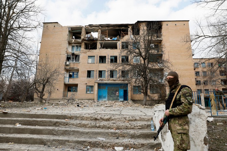A photo of a solider standing guard in front of a damaged building.