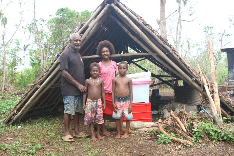 A couple with two children standing outside their A-frame shaped home in Vanuatu