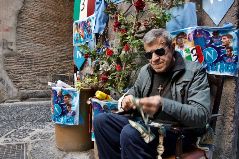 Umberto Iannaccone sits and cuts out pieces of fabric for his hand made collage of Jesus. Umberto set up a space between two buildings in Napoli’s historic centre to honor the Napoli team.