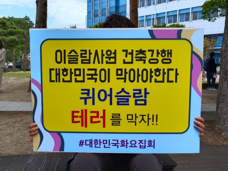 Anti-mosque protester outside the Buk district office holds a banner that reads: ""The Republic of Korea must stop the forceful construction of the mosque. We must stop queerslam terrorism." The placard covers their face