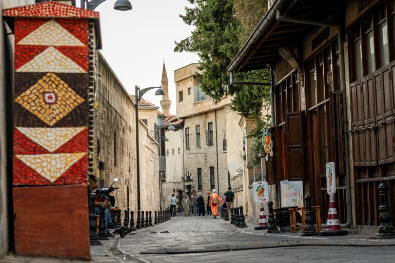A photo of a street with people at the end of it and a mosaic with geometric patterns on one of the buildings.