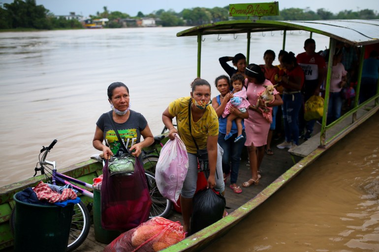 People carrying bags of clothes and belongings arrive on a long wooden canoe across a brown river.