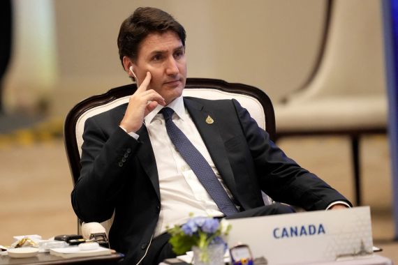 Justin Trudeau sits at the APEC conference behind a sign that reads "Canada"