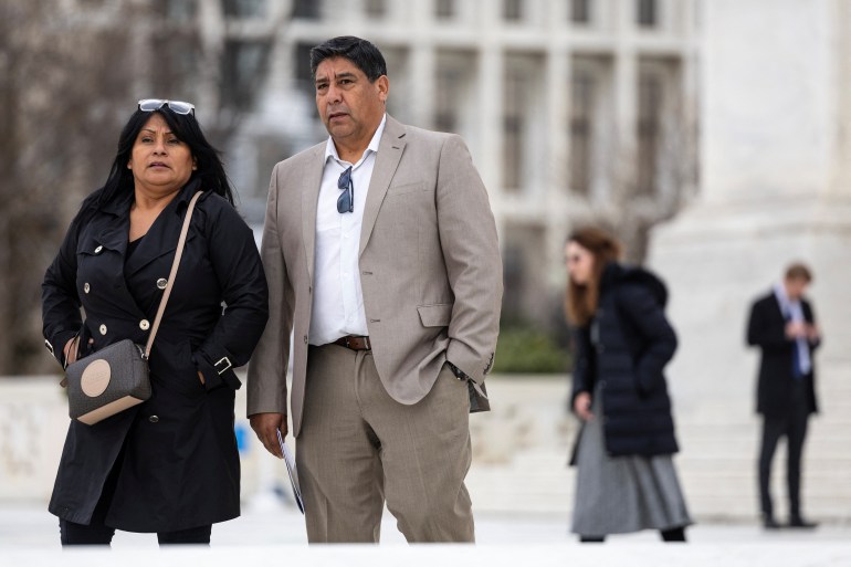 A couple, one in a black dress and the other in a tan suit, are seen outside the Supreme Court.