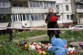 A woman pays tribute to civilian people killed by a Russian missile attack, amid Russia's attack on Ukraine, in the town of Uman, Cherkasy region, Ukraine April 29, 2023. The woman is holding a bouquet or red poppies and standing before a makeshift memorial made up of flowers and stuffed animals.