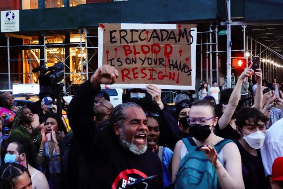 Protesters hold up a hand-painted sign that reads: "Eric Adams: Blood is on your hands. Resign"