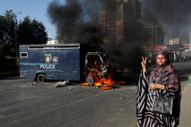 A woman gestures next to a burning police vehicle during a protest by the supporters of Pakistan's former Prime Minister Imran Khan after his arrest, in Karachi