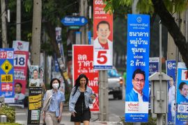 Two women walking past campaign banners hanging from lamp posts in Bangkok.