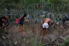 Migrants and refugees try to climb a fence on the US-Mexico border