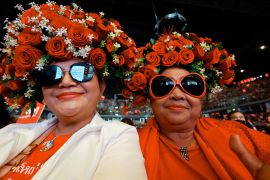 Pheu Thai supporters wearing red flowers in their hair and sunglasses. They are smiling.