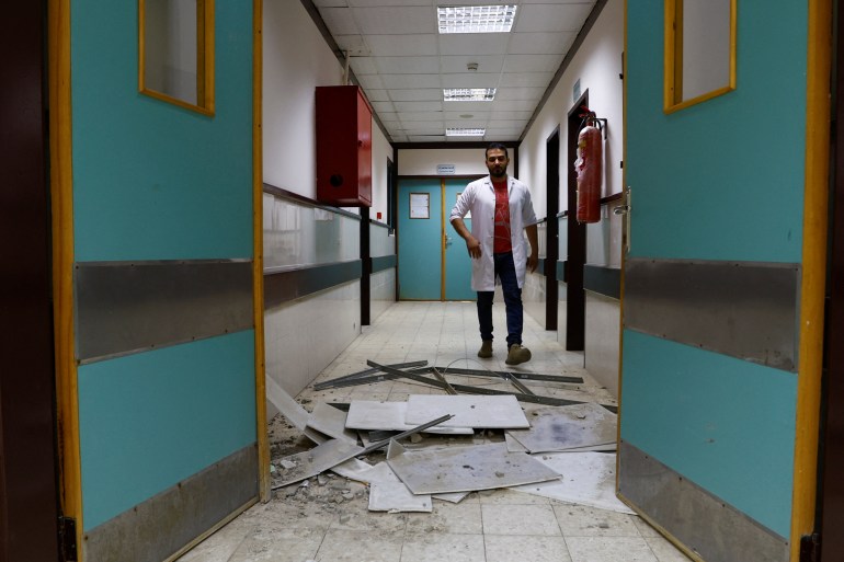 A man walks as Palestinians inspect a hospital damaged in a nearby Israeli strike, in the central Gaza Strip. 