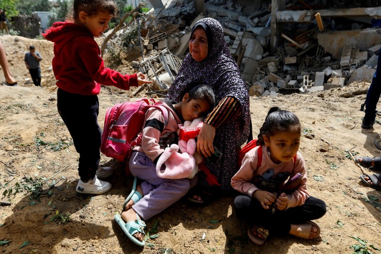 A Palestinian woman, Fatima Bashir, and her granddaughters sit beside the remains of their house which was destroyed in Israeli air strikes, in Deir al-Balah town in the central Gaza Strip.