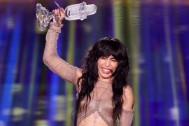 Loreen from Sweden appears on stage after winning the 2023 Eurovision Song Contest in Liverpool, the United Kingdom. She is smiling while holding up the glass microphone trophy over her head.