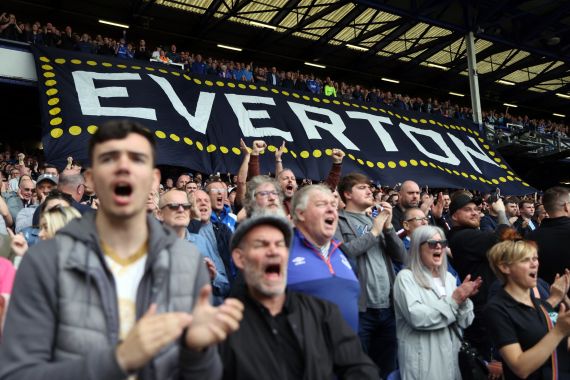 Everton fans inside the stadium before a match with a banner reading 'Everton' in the background