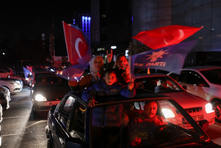 AK supporters passing hear the HQ in their cars wave flags. It's dark.
