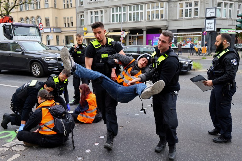 Police officers carry away an activist of the "Letzte Generation" (Last Generation), who previously glued himself to a street at Steglitz district to protest for climate councils, a speed limit on highways as well as for affordable public transport, in Berlin, Germany May 16, 2023