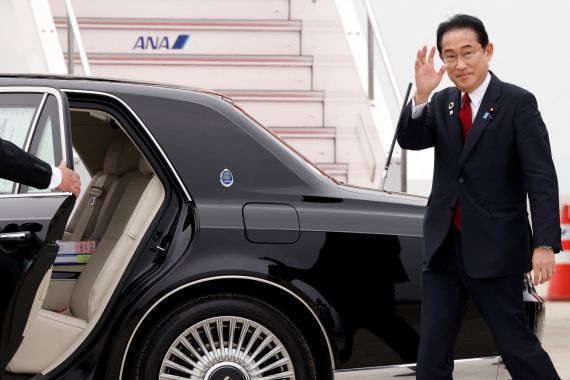 Japanese PM Fumio Kishida waves as he walks to a waiting black limousine after getting off a plane at Hiroshima airport, He is smiling.