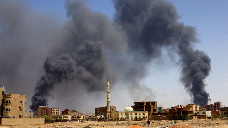 A man walks while smoke rises above buildings after aerial bombardment
