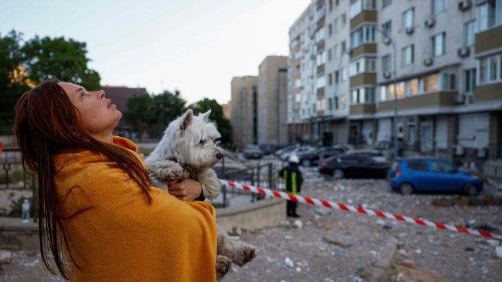 A woman with a dog looks at her apartment building heavily damaged during a massive Russian drone strike