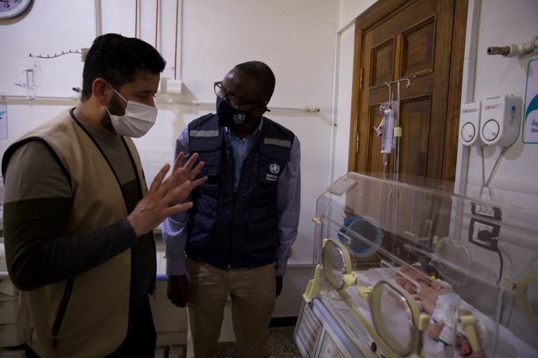 Two men stand next to a baby in an incubator