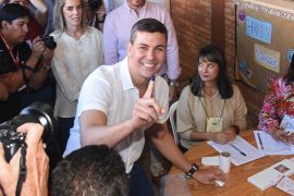 Santiago Pena shows his ink-stained finger after voting in the election. He is smiling,