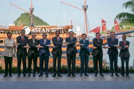 ASEAN leaders crossing arms for a 'family photo' at their summit in Labuan Bajo. There is a sailing ship behind them.