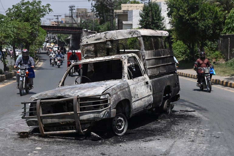 Commuters ride past a burnt vehicle set on fire during a protest by Pakistan Tehreek-e-Insaf party activists and supporters of former Pakistan's Prime Minister Imran Khan over the arrest of their leader
