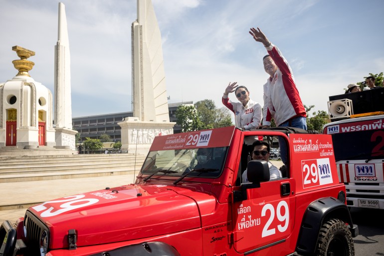 Pheu Thai Party's Party's Paetongtarn Shinawatra (left) and Srettha Thavisin (right) ride in an open top car past Bangkok's Democracy Monument. The car is painted red and has the party number - 29 - in white on the side