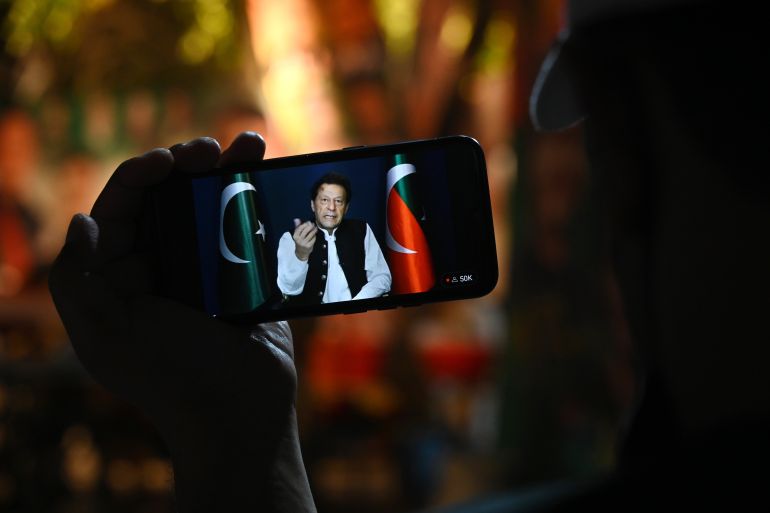 A member of Tehreek-e-Insaf party listens to Khan's speech on a phone, in Zaman Park, Lahore