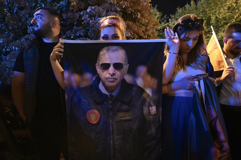 A supporter displays a poster of incumbent President Recep Tayyip Erdogan wearing aviator glasses and looking serious.