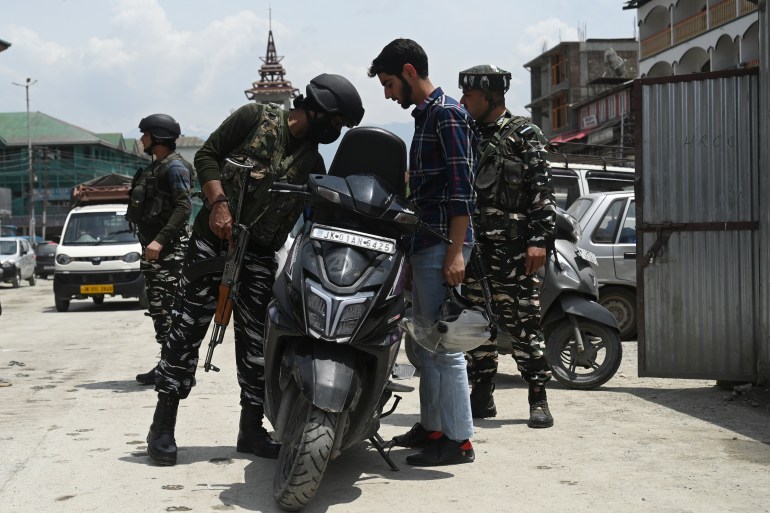 Indian paramilitary troopers search the scooter of a motorcyclist along a street in Srinagar
