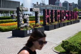 A woman walks past a "G7 Hiroshima" flower sign at the Peace Memorial Park in Hiroshima, Japan, ahead of the G7 Leaders' Summit, on May 17, 2023. It is sunny and the flowers are white and red.
