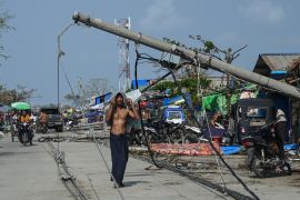 A man walks near a fallen pylon on a damaged Sittwe street. He is bare chested.